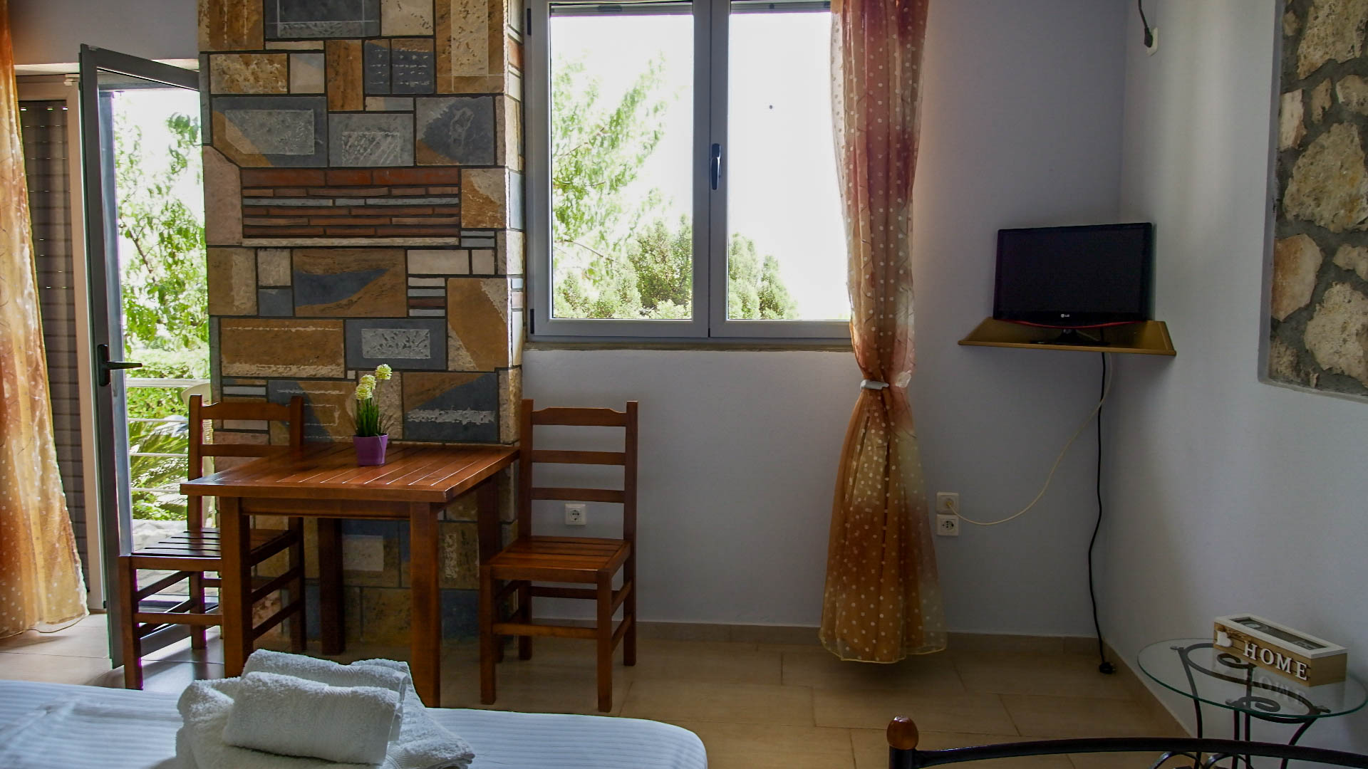 A wooden table with two chairs next to the window and a small tv on the right.